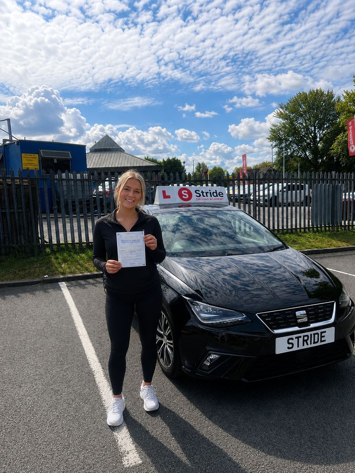 A Stride pupil with their practical driving test pass certificate beside the Stride car