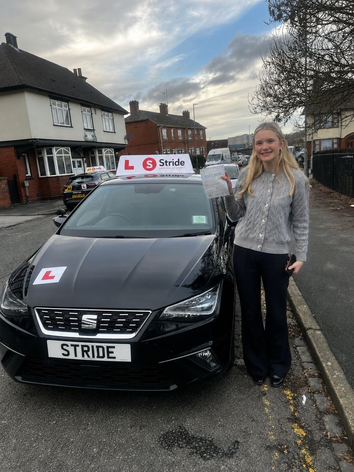 A Stride pupil with their practical driving test pass certificate beside the Stride car